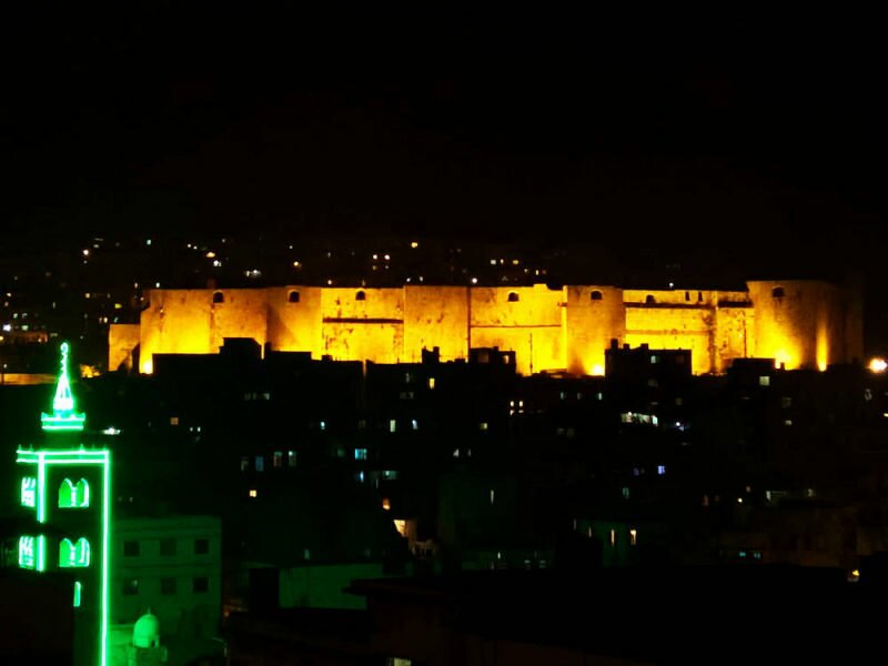 Night view of the western facade of the Tripoli Citadel (back). The minaret of the Great Mansouri Mosque (front left).